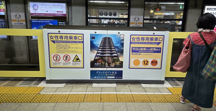 Boarding platform in Japan with signs for Women Only Car and a building advertisement.