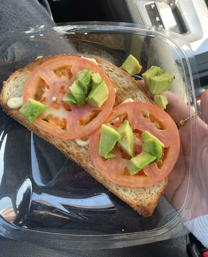 Open sandwich with sparse tomato and avocado, highlighting infuriating food scams in a plastic container.