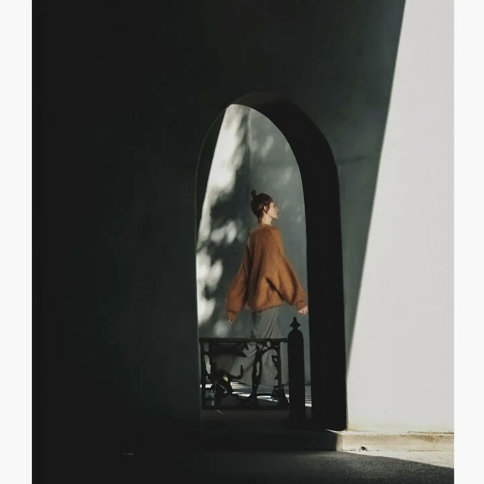 Minimalist photo of a woman in a brown sweater walking through a shadowed archway, capturing a quiet side of Tokyo.