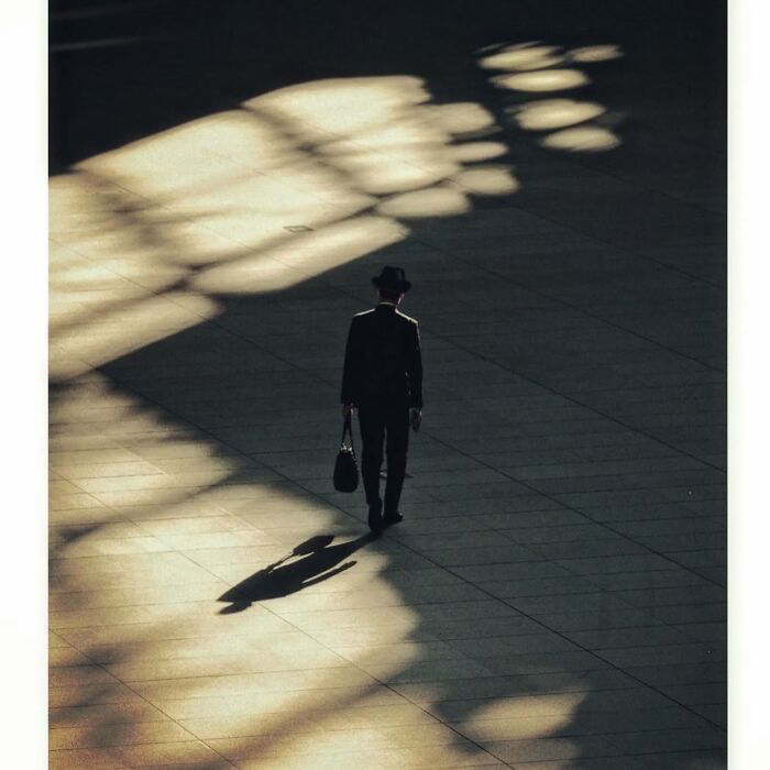 A minimalist shot of a man in Tokyo walking through dramatic shadows, capturing a quiet, hidden side.