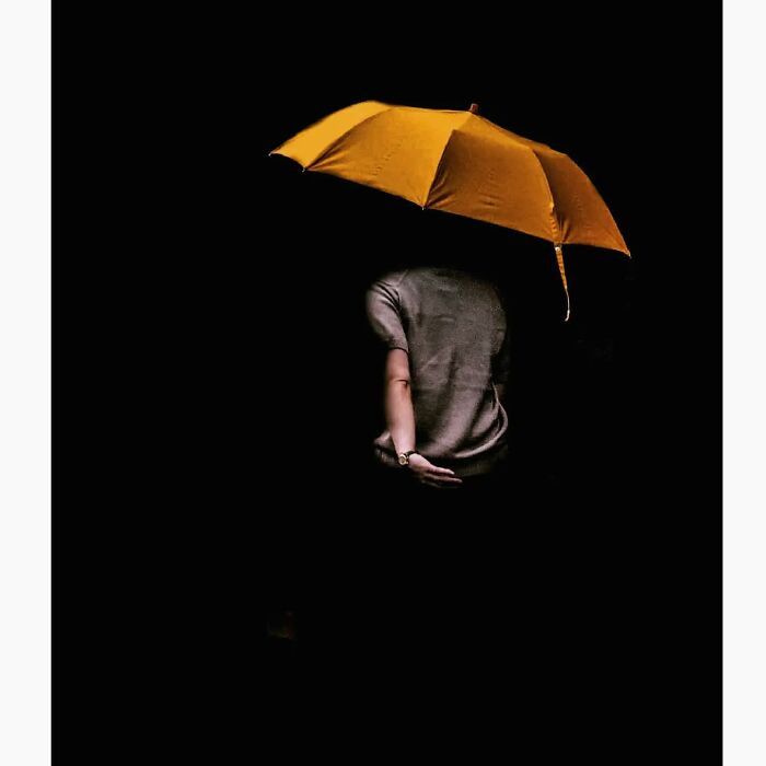 Minimalist image of a person holding a yellow umbrella in a dark, quiet setting, representing a hidden side of Tokyo.