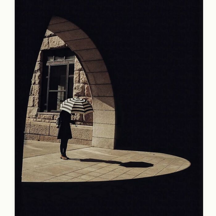 Minimalist shot of a person with a striped umbrella in a shadowed archway in Tokyo.