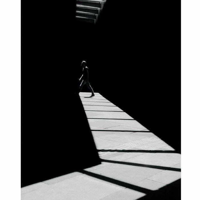 Minimalist shot of a person walking through a narrow sunlit path in Tokyo.