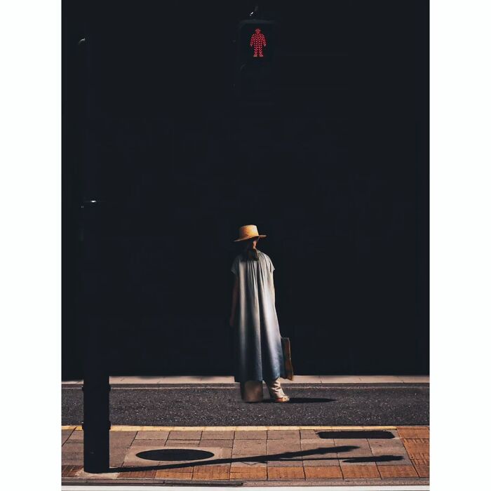 Minimalist shot of Tokyo; a person in a hat stands beneath a red pedestrian light, casting a shadow on the street.