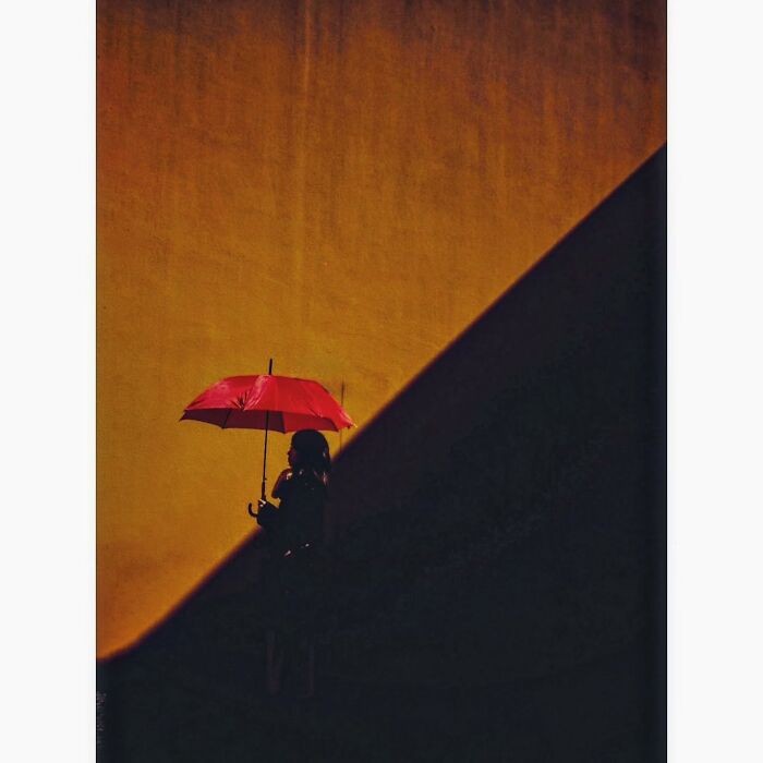 Minimalist shot of a person holding a red umbrella against a stark yellow and black background in Tokyo.