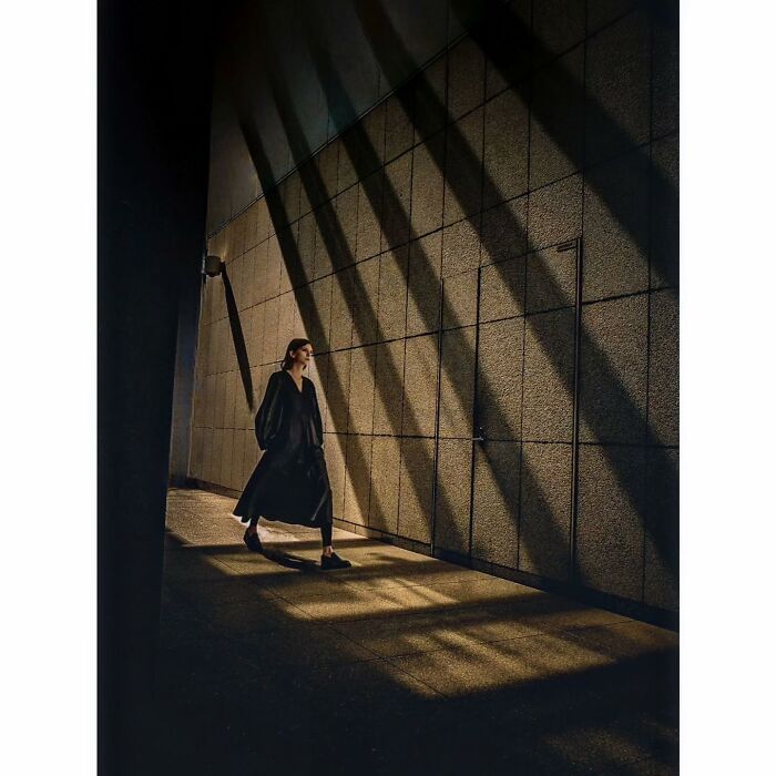 Minimalist photo of a person walking along a shadowed, textured wall in a quiet corner of Tokyo.