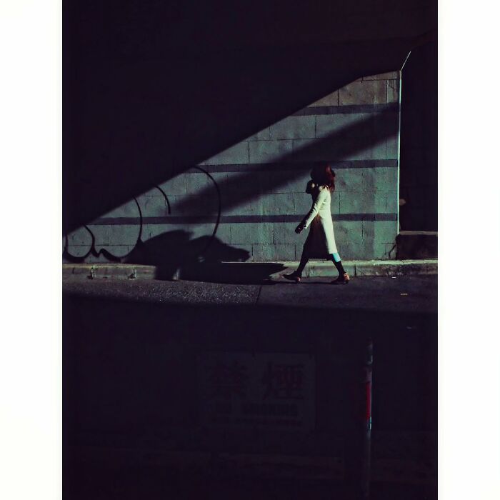 A woman walks in the shadows of a Tokyo street, showcasing a minimalist, hidden side of the city.