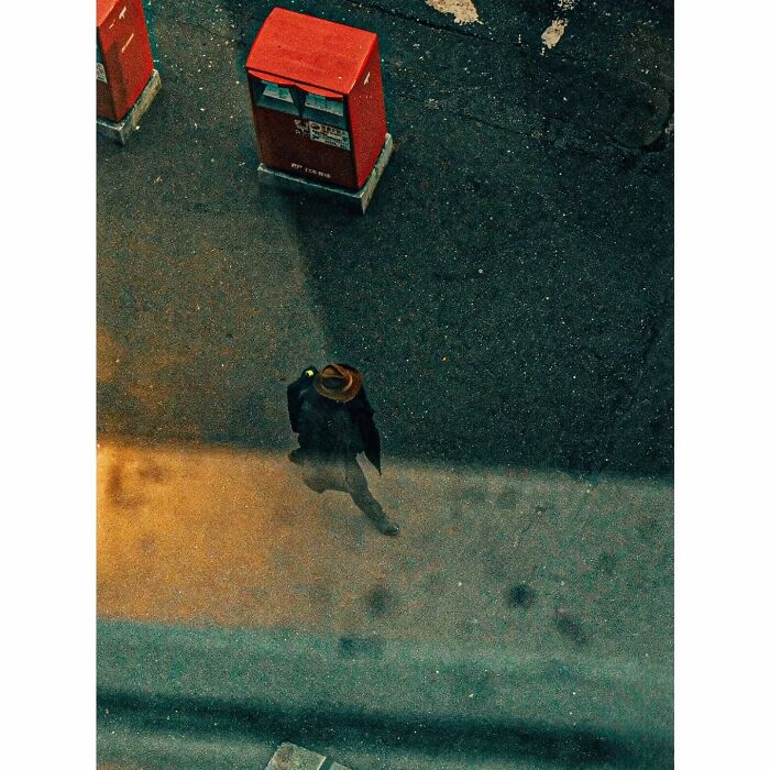 Minimalist shot of a person walking quietly on a street in Tokyo, viewed from above, near red mailboxes.