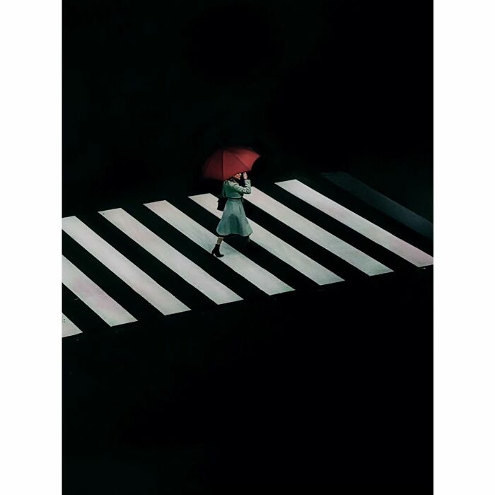 Person with red umbrella on Tokyo crosswalk at night, showcasing minimalist photography style.