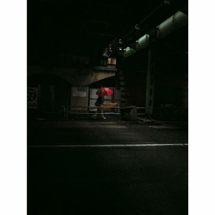 Person with red umbrella walking through a dimly lit street in Tokyo, capturing a minimalist and quiet scene.