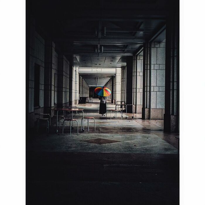 Minimalist shot of Tokyo; a person with a colorful umbrella stands in a dimly lit, empty corridor.