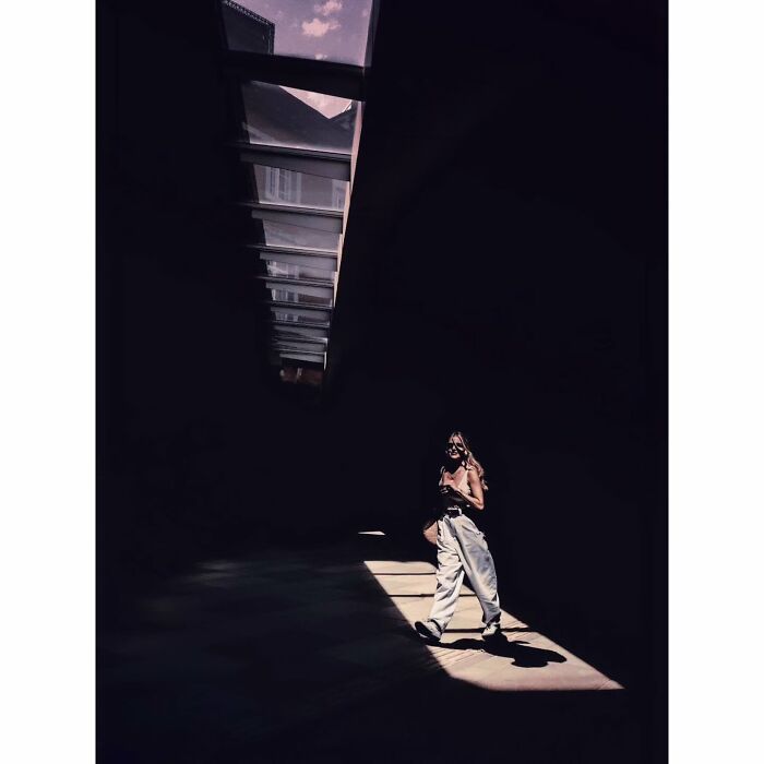 Minimalist shot of a person walking in a dimly lit passageway in Tokyo, under a skylight, capturing a quiet moment.