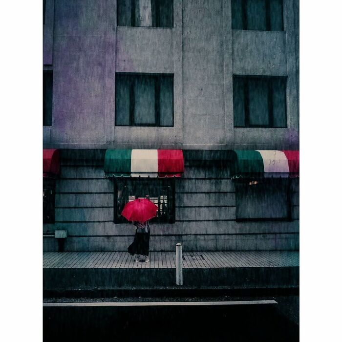 Minimalist Tokyo: Person with red umbrella walks past colorful awnings on a rainy street.