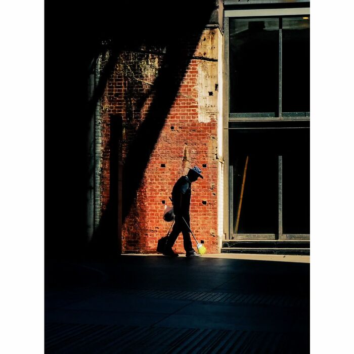 Man walking in shadow against a brick wall in Tokyo, showcasing minimalist photography style.