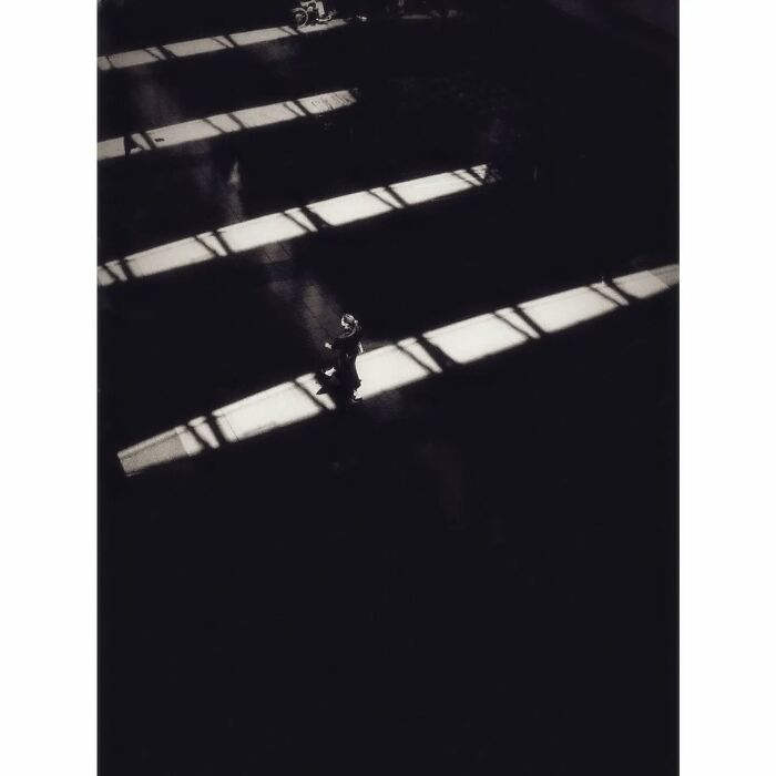 A lone figure walks through shadows in Tokyo, captured in a minimalist black-and-white style.