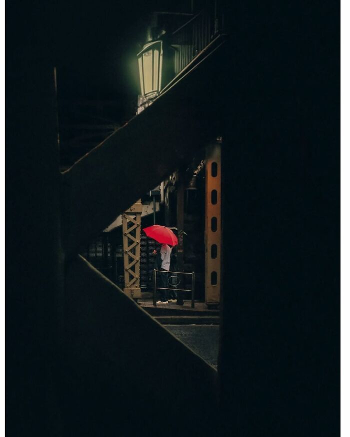 Minimalist shot of Tokyo, featuring a person with a red umbrella standing under a streetlamp at night.