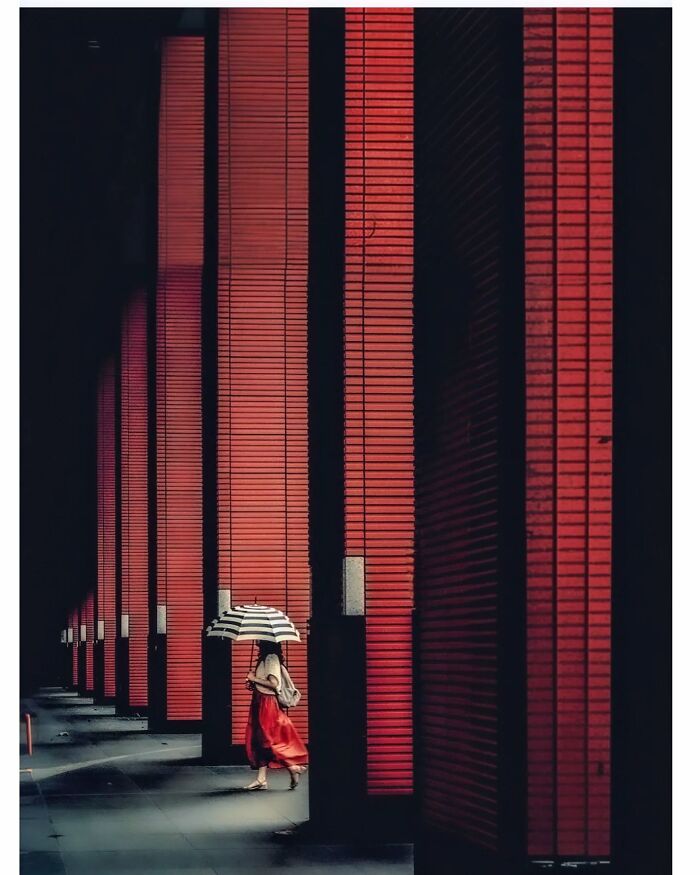 Minimalist shot of a person with an umbrella walking by red columns, capturing Tokyo's quiet side.