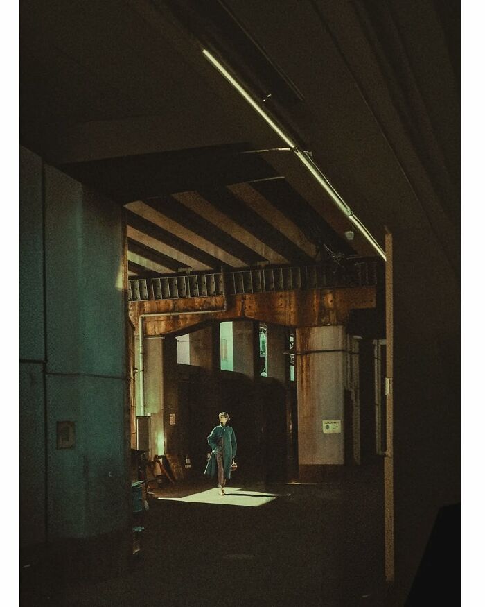 Minimalist shot of a person walking through a dimly lit, hidden area under an overpass in Tokyo.