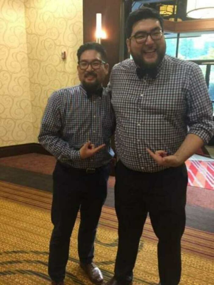 Two men wearing identical checkered shirts and bow ties, standing together and pointing at each other, creating a mildly interesting scene.