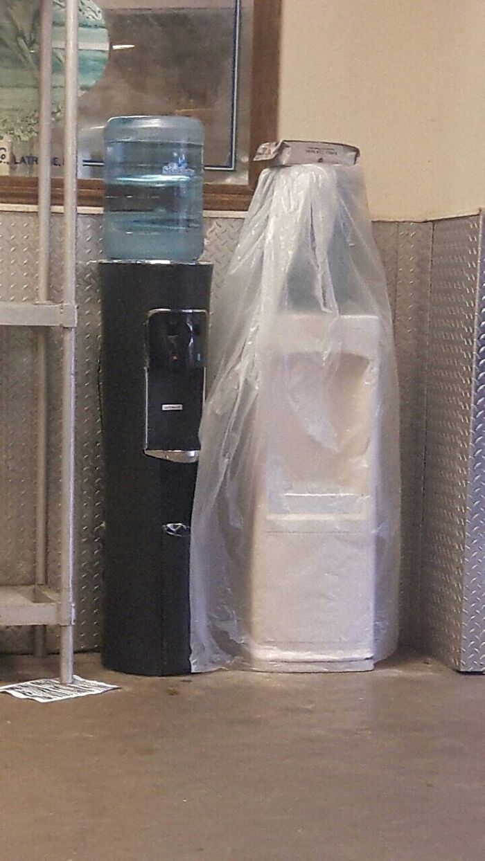 "Mildly interesting scene of two water coolers, one wrapped in plastic, placed side by side."