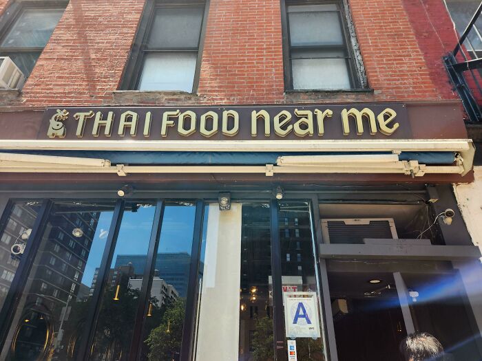 Sign reading "Thai Food Near Me" on a brick building, a mildly interesting restaurant name.
