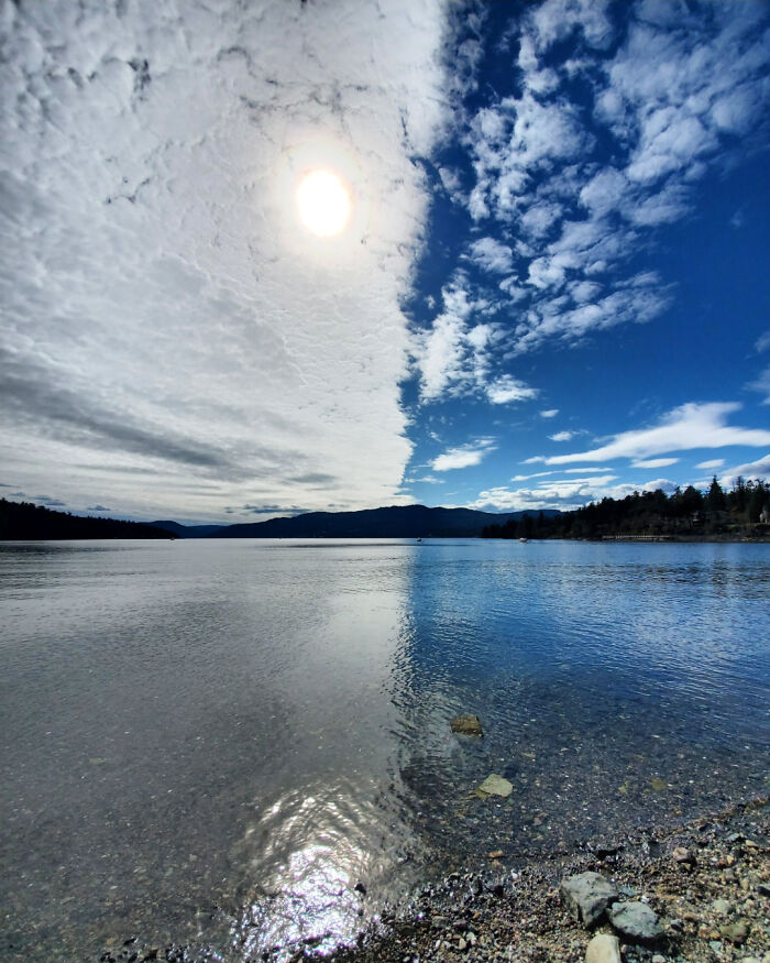 A mildly interesting view of a sky divided by clouds and clear blue, reflecting on a calm lake surface.