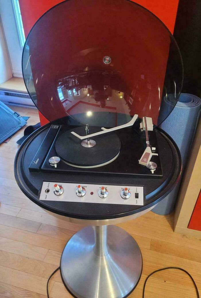 Cool-old-things: vintage record player with a sleek design, featuring a transparent lid, on a metallic pedestal stand.