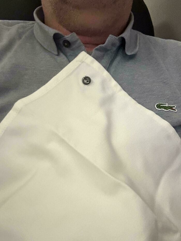 Man wearing a light grey polo shirt with a button and a white shirt laid over it, showcasing a mildly interesting detail.