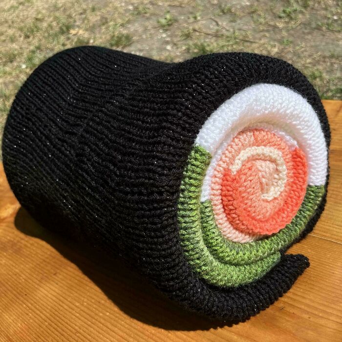 Knitted sushi roll resembling black seaweed and colorful filling, embodying a mildly interesting surprise.
