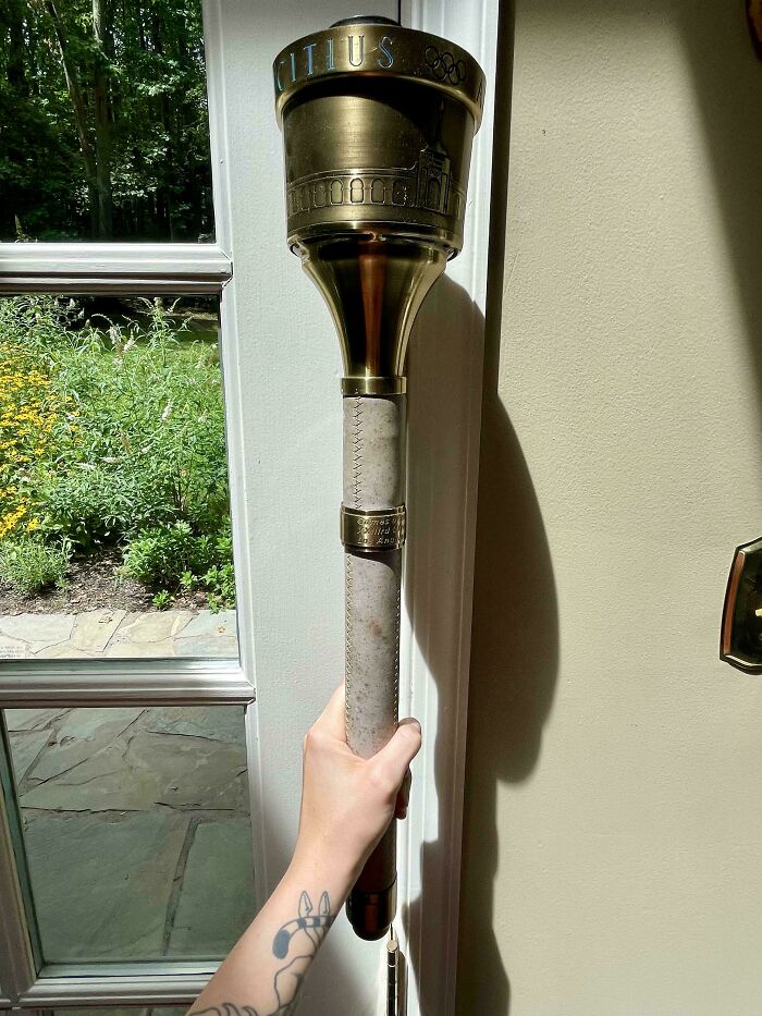 Hand holding an Olympic torch indoors, with a garden visible outside the window; a mildly interesting find.