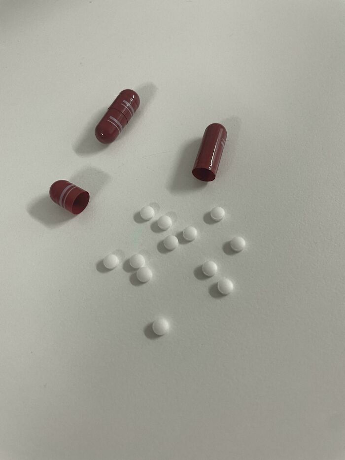 Empty reddish capsules with small white pills on a surface, demonstrating a mildly interesting composition.