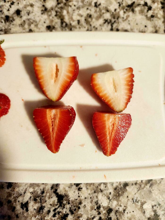 Strawberries cut in half display symmetrical patterns on a white cutting board.