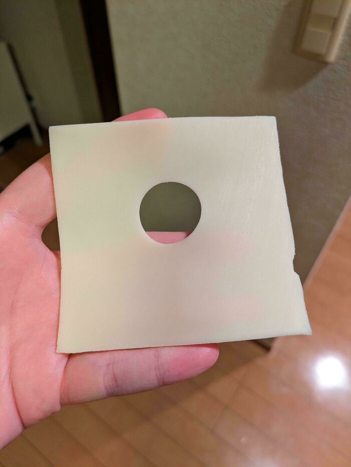 A hand holding a slice of cheese with a perfect round hole, mildly interesting and surprising detail.