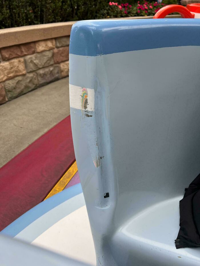 A mildly interesting detail of a worn sticker on a blue theme park ride seat, with stone and floral background.