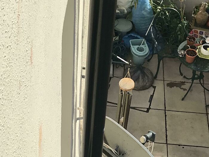 Messy balcony with clutter; wind chimes hanging, showing the presence of terrible neighbors.
