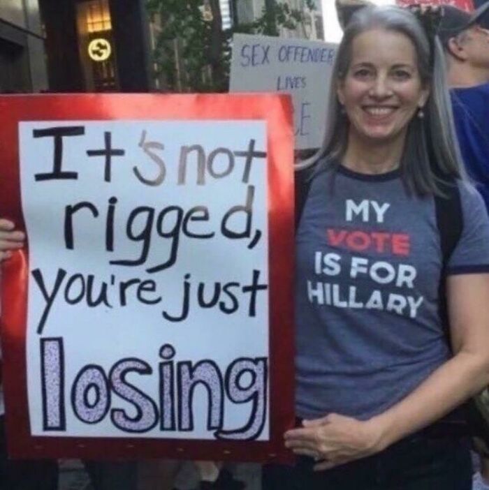 Woman holding a sign saying "It's not rigged, you're just losing," related to aged predictions.