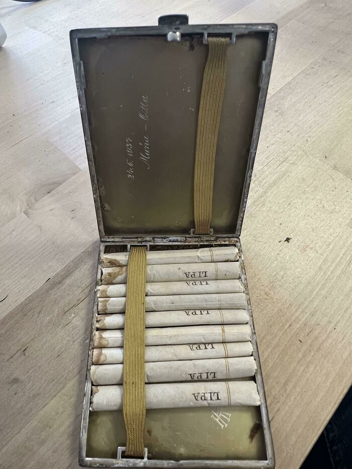 Cool-old-things: Vintage cigarette case with cigarettes secured by a strap, displayed on a wooden surface.