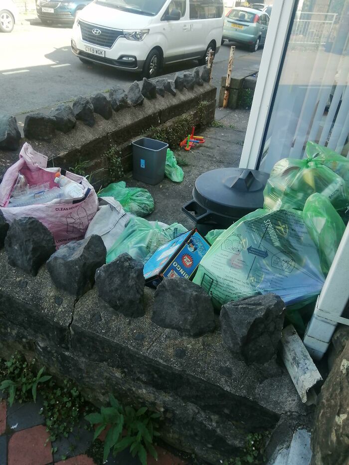 Messy front yard with piles of garbage bags and bins, illustrating issues with terrible neighbors in an urban setting.