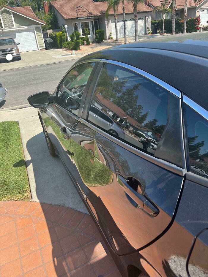 Car door dented badly in suburban driveway, showing horrific neighbor damage shaming in residential neighborhood.