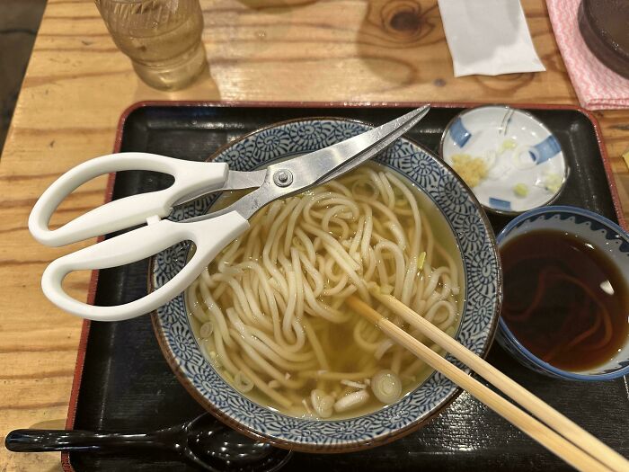 Bowl of noodles with scissors on the side, showcasing interesting Japan culinary presentation.