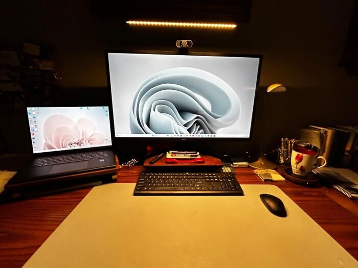 Work from home tech essentials on a desk: laptop, monitor, keyboard, mouse, and a mug.