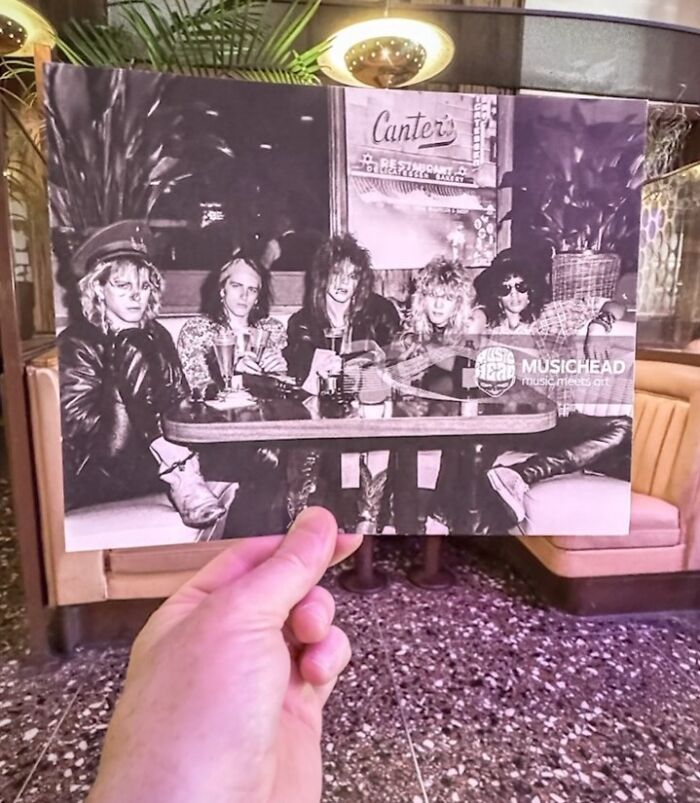 A hand holds a photo of iconic legends at Canter's, with a historic restaurant background.