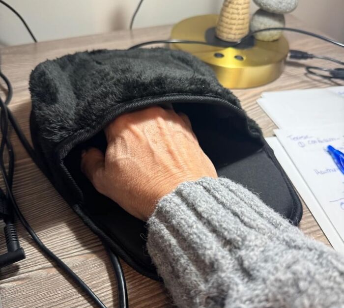A hand inside a heated mouse pad on a desk, showcasing work from home tech essentials.