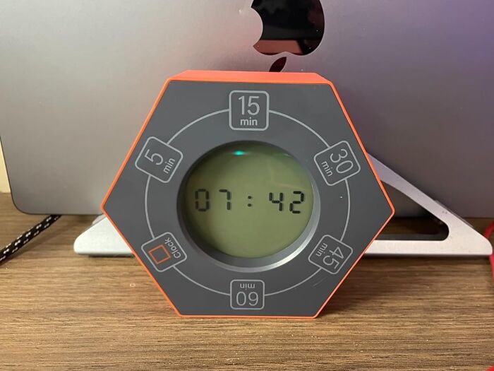 Digital timer in front of a laptop on a wooden desk, a work from home tech essential.