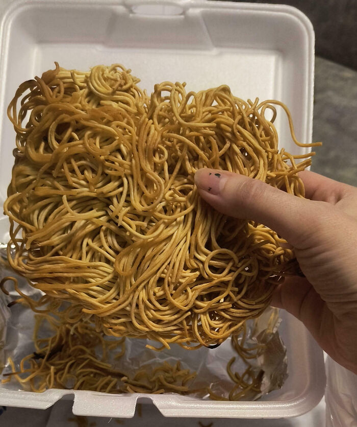 Hand holding a skimpy portion of crispy noodles in a takeout box, illustrating food scams.