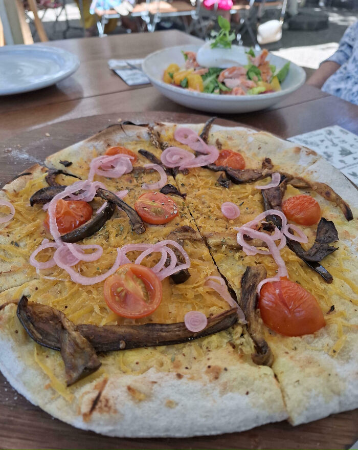 Pizza with minimal toppings, highlighting food scams with sparse onions and tomatoes.