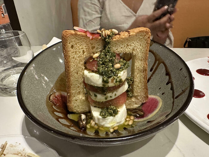 Stacked salad with pesto between two slices of toast, resembling a food scam.