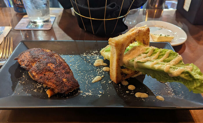 Unsubstantial portion of grilled meat and lettuce with a drizzle, highlighting questionable food presentation.