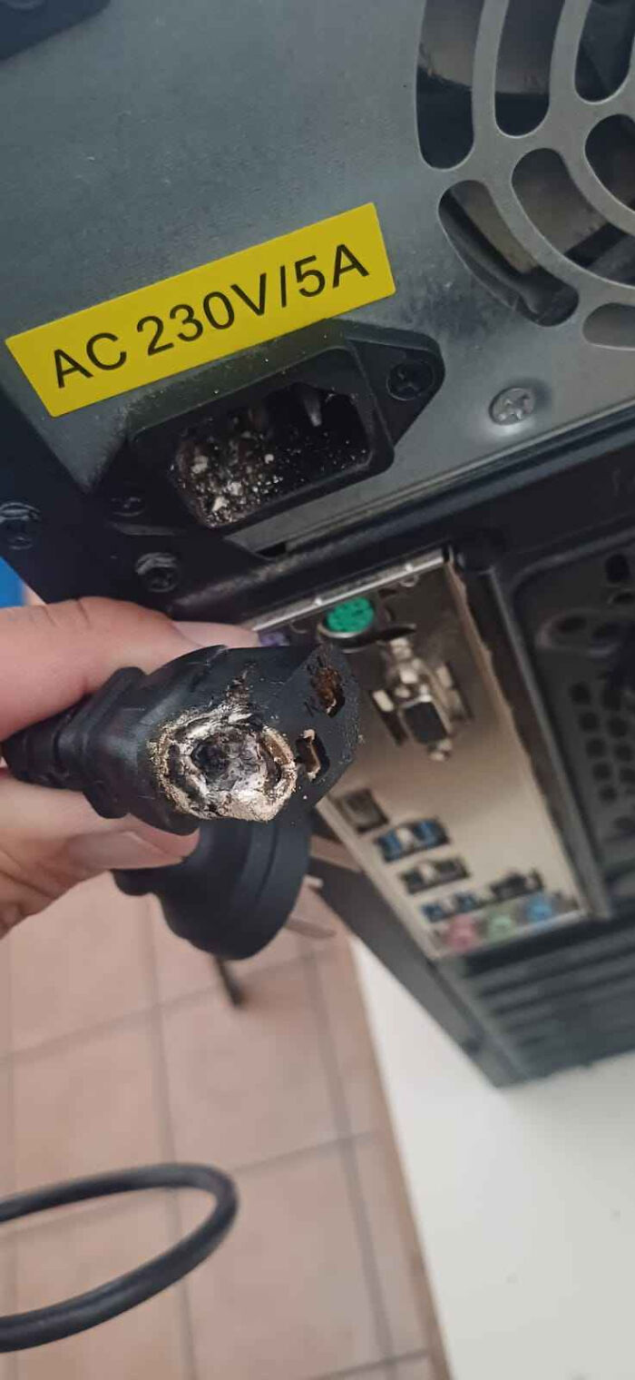 Burnt power cable plug held near computer power socket with AC 230V 5A label, illustrating tech support issues.