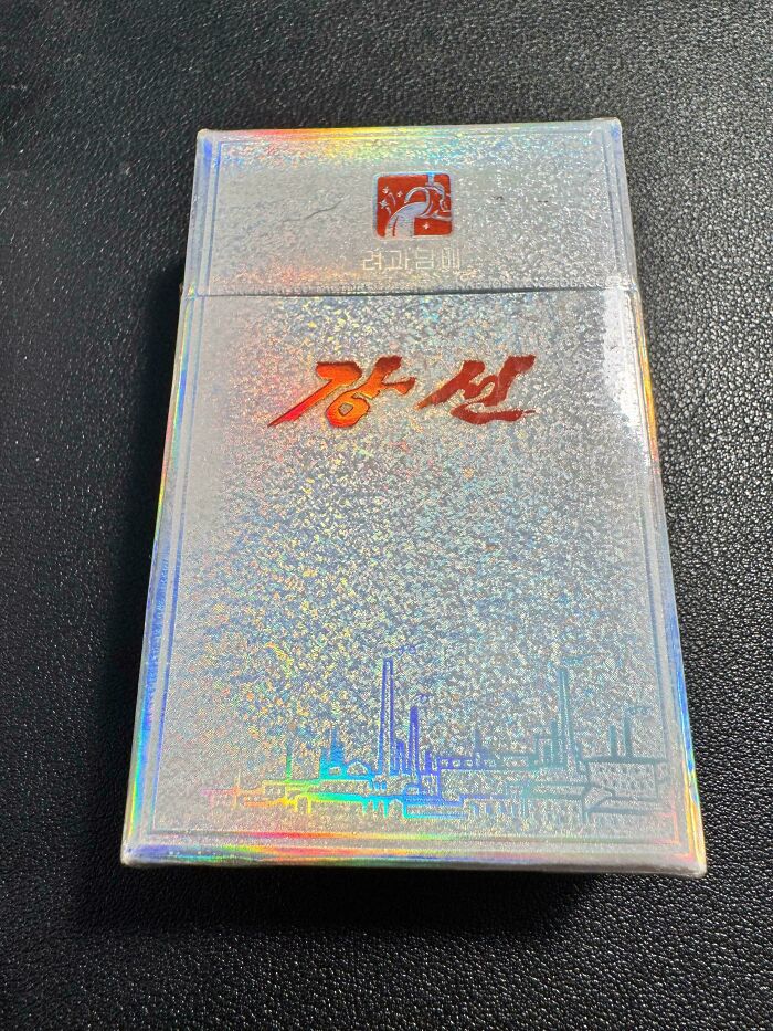 Holographic cigarette pack with red text and skyline design, reflecting mildly interesting light patterns.